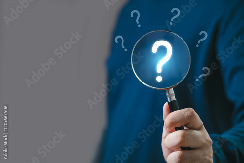 Photos Close-up of a hand holding a magnifying glass with question marks in the background, symbolizing search, inquiry, and problem-solving in a business context