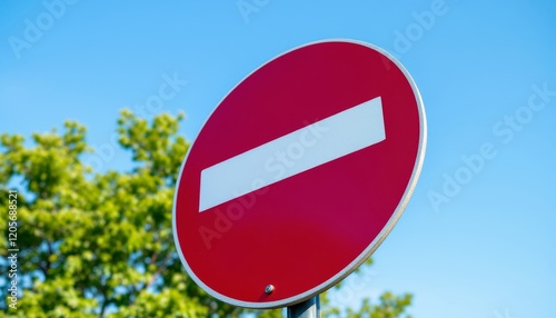 A red and white no entry road sign with green trees and clear blue sky background