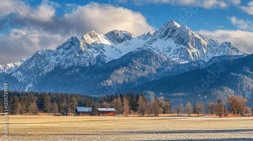 Snow capped mountains overlooking a field with two small buildings surrounded by trees photo