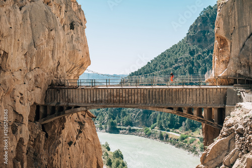 Lonely hiker woman standing on Hanging Bridge over the mountain river and enjoying Spanish Malaga province valey landscape during Caminito del Rey hiking tour in narrow Canyon. South Spain.