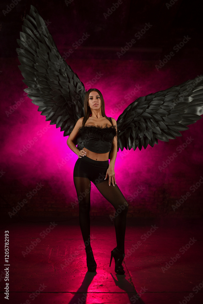 Beautiful girl in a black corset and black tights with black angel wings on pink smoky background. Beautiful girl in a black corset and black tights with black angel wings on pink smoky background.