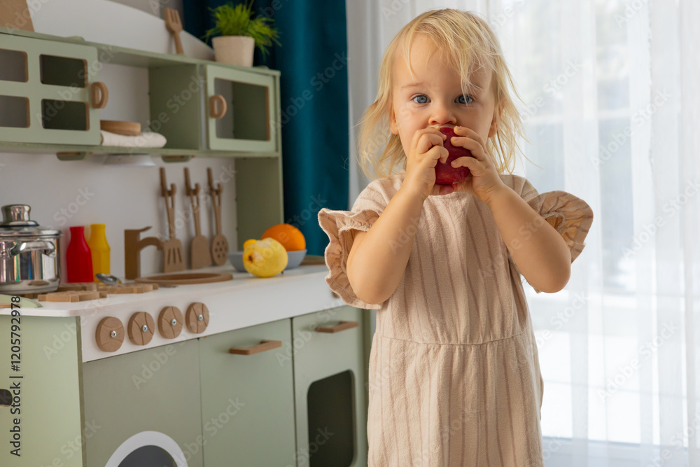 Child playing in a toy kitchen with a red apple during a bright indoor daytime setting Child playing in a toy kitchen with a red apple during a bright indoor daytime setting