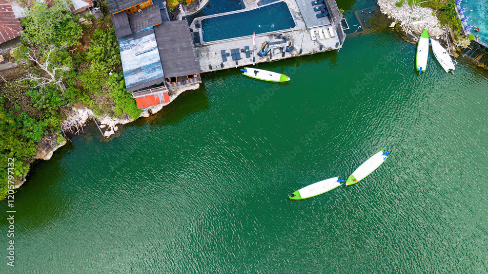 Aerial shot of white paddleboards with green accents floating on emerald-green volcanic lake waters, showcasing the contrast against the dark wooden deck structure