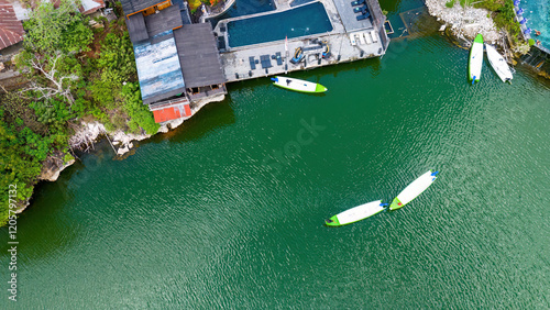 Obraz na płótnie Aerial shot of white paddleboards with green accents floating on emerald-green volcanic lake waters, showcasing the contrast against the dark wooden deck structure w salonie