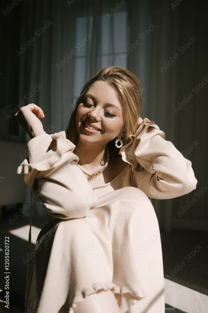Beautiful blonde woman posing near the window in the sun rays in a beautiful modern stylish beige interior