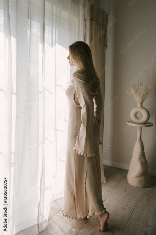 Beautiful blonde woman posing near the window in the sun rays in a beautiful modern stylish beige interior