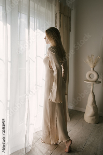 Beautiful blonde woman posing near the window in the sun rays in a beautiful modern stylish beige interior