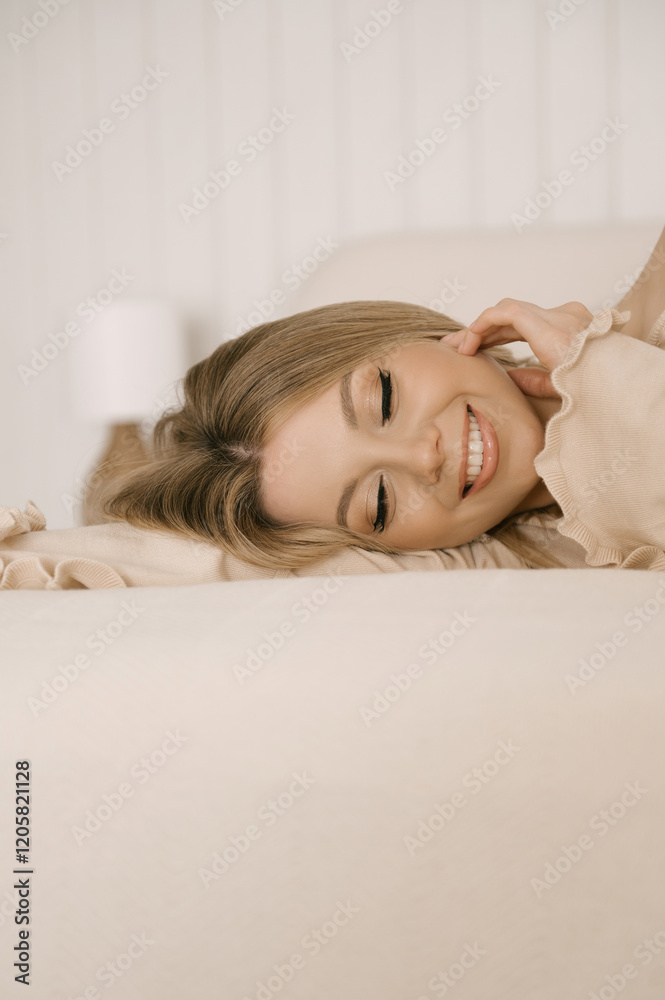Beautiful blonde woman posing on light bed in modern stylish beige interior
