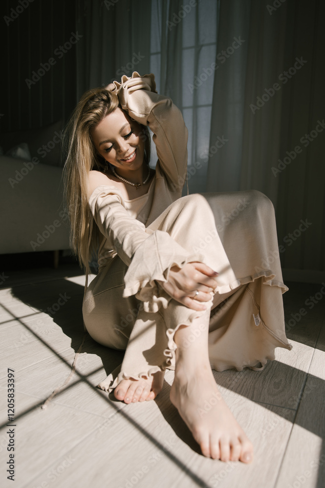 Beautiful blonde woman posing near the window in the sun rays in a beautiful modern stylish beige interior