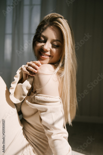 Beautiful blonde woman posing near the window in the sun rays in a beautiful modern stylish beige interior