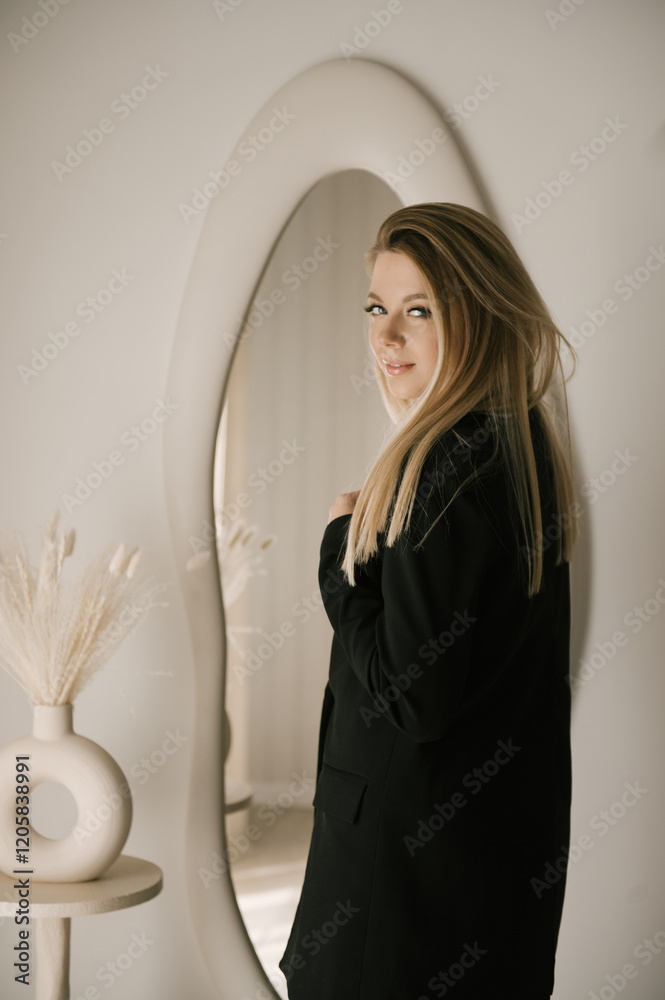 Beautiful blonde woman posing in beautiful modern stylish beige interior on photo of large mirror
