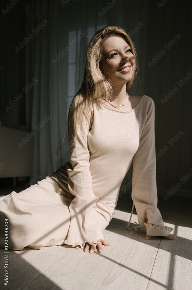 Beautiful blonde woman posing near the window in the sun rays in a beautiful modern stylish beige interior