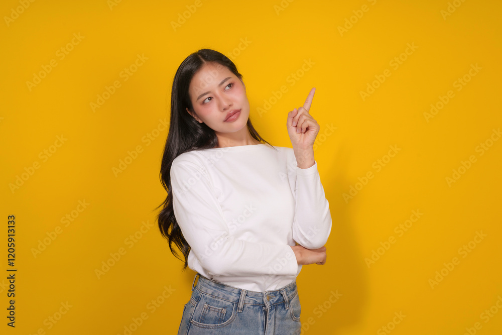 Young woman pointing her finger up and looking at the top right corner, expressing a new idea on a yellow background Young woman pointing her finger up and looking at the top right corner, expressing a new idea on a yellow background