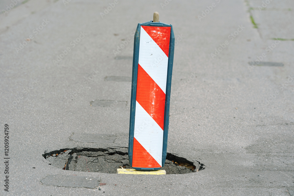 Close-up of reflective warning sign covering pothole on the pavement, importance of street maintenance and public safety. Urban road damage and alerting drivers and pedestrians to potential hazards