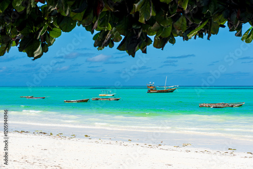 Plage de zanzibar avec des bateaux de pêche et de tourisme, eaux turquoise, sous des feuillages pour l'ombre photo