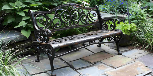 Ornate black metal bench on a stone patio surrounded by green plants