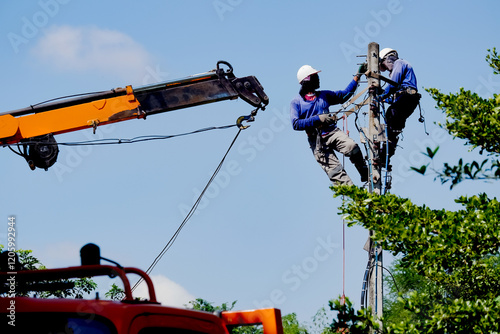 Workers on low-voltage electric poles have safety equipment, steel cranes and ladders.