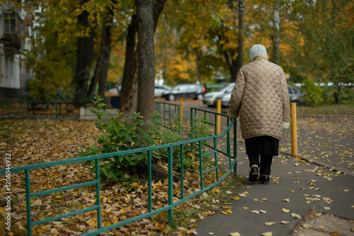 Grandma walks down autumn street. Old woman in Russia in autumn. Walk of elderly person near house.