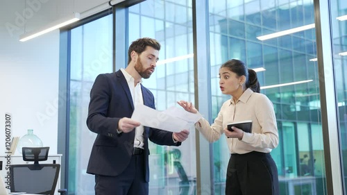 Two angry co-workers, a man and a woman arguing intensely in a modern office setting, showcasing conflict and emotion during heated business discussion or disagreement. Colleagues arguing, quarreling
