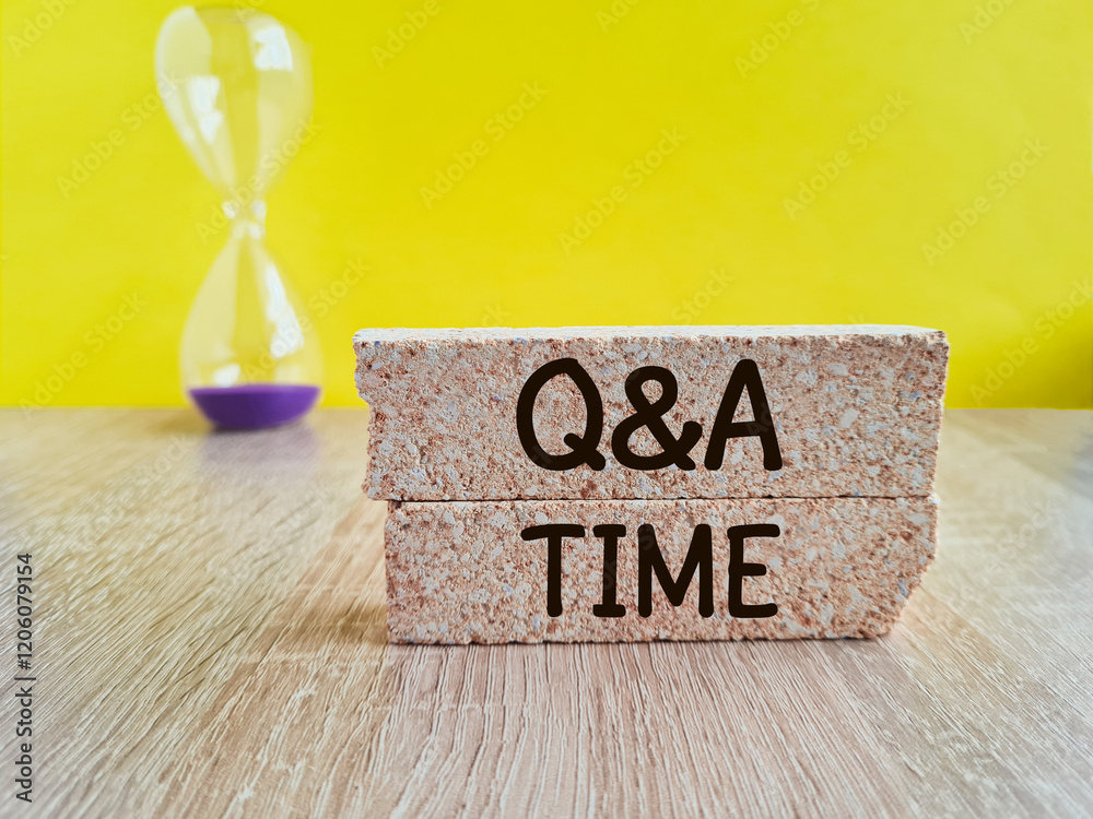 Q and A, questions and answers time symbol. Concept words 'Q and A time' on brick blocks on a wooden table. Hourglass. Yellow background. Business and Q and A time concept.