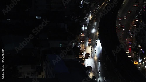 Aerial view footage of a dimly light urban street at night. Bangkok traffic road in night time showing less vehicles on colorful light vibe cities top view. Night cityscape road traffic aerial view.