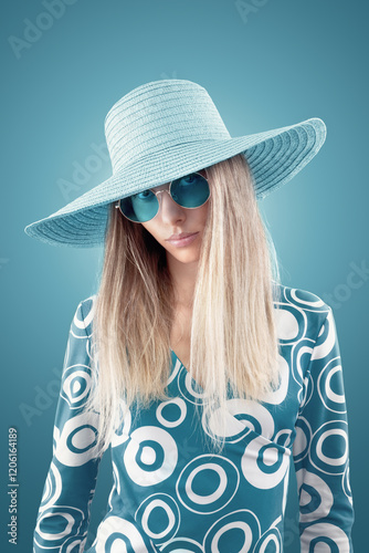Fashion portrait of beautiful young blonde woman wearing sunglasses and summer hat, isolated on blue background. For magazine cover, advertising poster or web banner for vacation and travel concepts