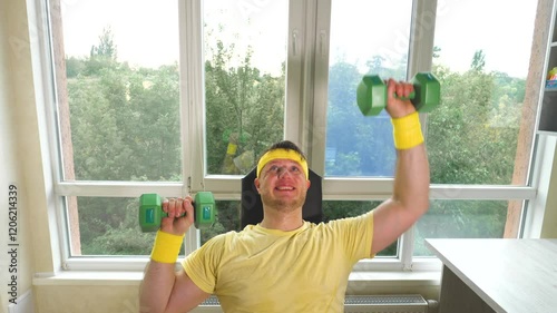 Home workout with dumbbells, a young guy pumps his shoulder muscle with a smile. Workout at home. Slow motion