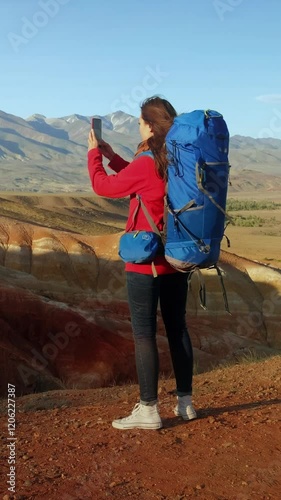 Vertical Video. Woman hiker on top of the mountain takes a photo. Female traveler takes a photo on a modern smartphone, makes beautiful pictures of beautiful mountain landscapes.