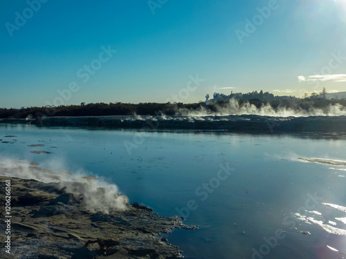 Geothermal area with steam rising from vents and hot springs along shoreline of Rotorua lake, Bay of Plenty Region, North Island New Zealand. Sky is clear blue. mineral-rich wet sand and mudflats