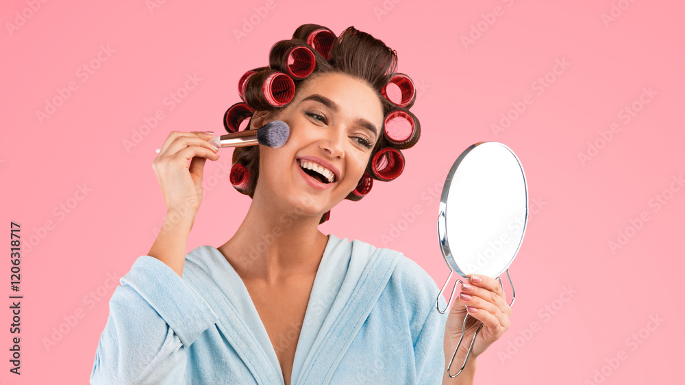 Joyful Housewife Making Makeup Using Cosmetic Brush And Round Mirror Standing On Yellow Studio Background. Woman With Hair Curlers Appyling Powder Cosmetics. Female Beauty, Make-Up Concept. Panorama Joyful Housewife Making Makeup Using Cosmetic Brush And Round Mirror Standing On Yellow Studio Background. Woman With Hair Curlers Appyling Powder Cosmetics. Female Beauty, Make-Up Concept. Panorama