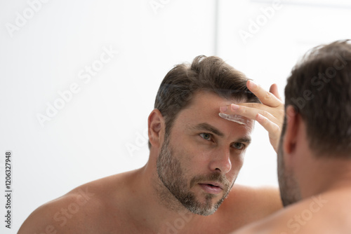 Handsome Man Applying Face Cream in the Bathroom. Closeup beauty portrait of satisfied young man after facial cream. Attractive brunet guy touching skin. Male coscmetic and beauty concept photo