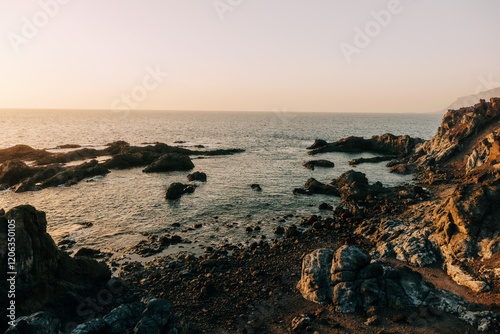 Rocky coastal landscape with calm sea and soft golden light