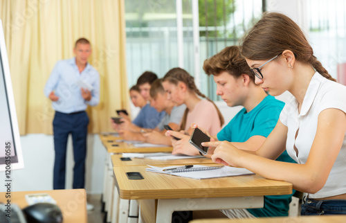 Teenager students sitting in class room and using their smartphones.
