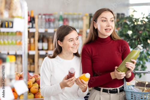 Foto Glad teeny girl and mom trying to choose the best smoothie in grocery shop