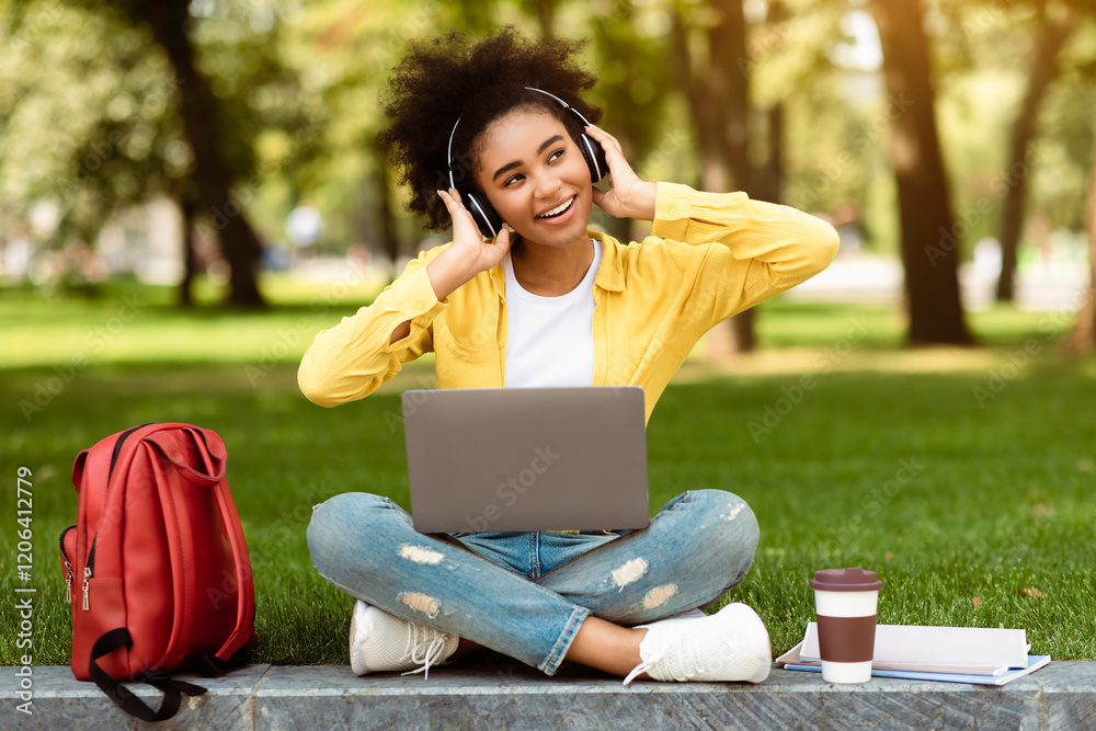 E-Learning. Happy Teenager Girl Using Laptop Computer Wearing Headphones Listening To Music Relaxing After Lecture Sitting In University Campus Park. Female Student Learning Online E-Learning. Happy Teenager Girl Using Laptop Computer Wearing Headphones Listening To Music Relaxing After Lecture Sitting In University Campus Park. Female Student Learning Online