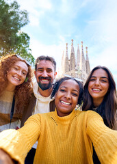 Vertical. Group diverse funny young tourist friends posing piggyback with hands joined in air taking selfie together in front of Sagrada Familia in Barcelona. Happy people enjoy holidays outdoor