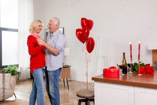 loving elderly couple of seniors celebrate Valentine's Day at home and dance the waltz, old man congratulates his wife with flowers and wine, pensioners on romantic date photo