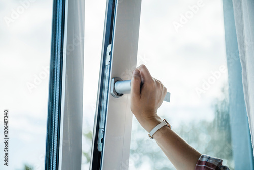 A professional close-up of a woman right hand turning the handle to tilt a luxury PVC window, highlighting superior craftsmanship, durability, and modern functionality. photo