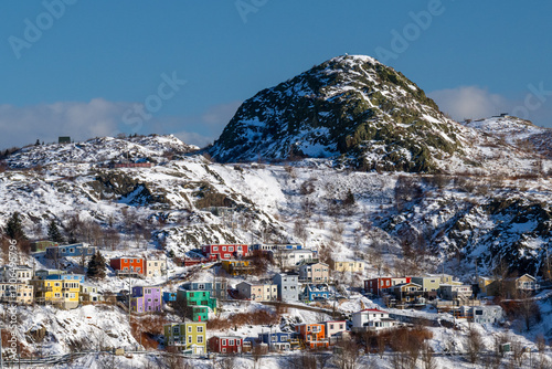 The hillside of historic St. John’s, Newfoundland with colorful wooden houses built on a cliff in winter. The ground is covered with fresh white snow. The vibrant residential buildings are picturesque