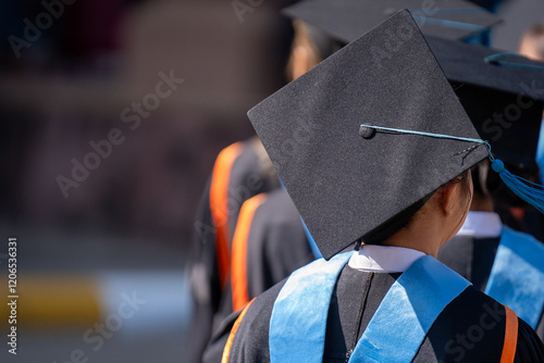 A group of people wearing graduation caps and gowns. The person in the middle is wearing a black cap with a blue ribbon