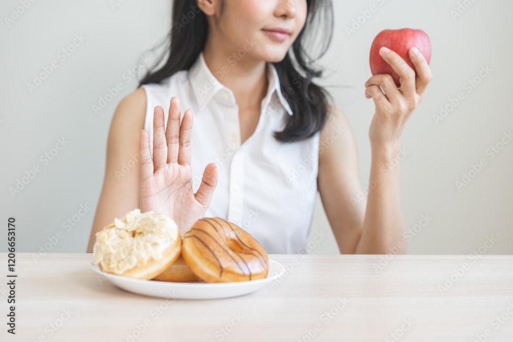 Diet asian young woman hand push out, refuse sugar donut, doughnut and sweet taste on plate and choose red apple for good health, fighting to keep it from getting fat. Healthy nutrition of weight loss Diet asian young woman hand push out, refuse sugar donut, doughnut and sweet taste on plate and choose red apple for good health, fighting to keep it from getting fat. Healthy nutrition of weight loss