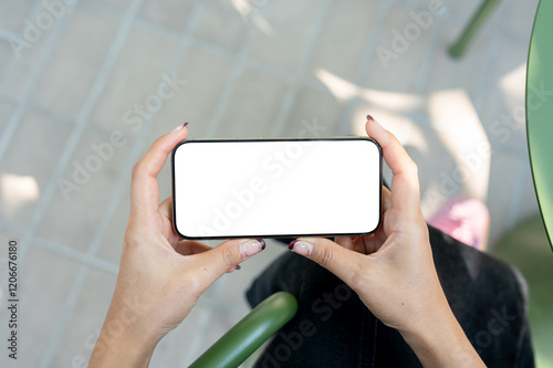 A woman holding a smartphone in a horizontal position, watching a video while sitting outdoors.