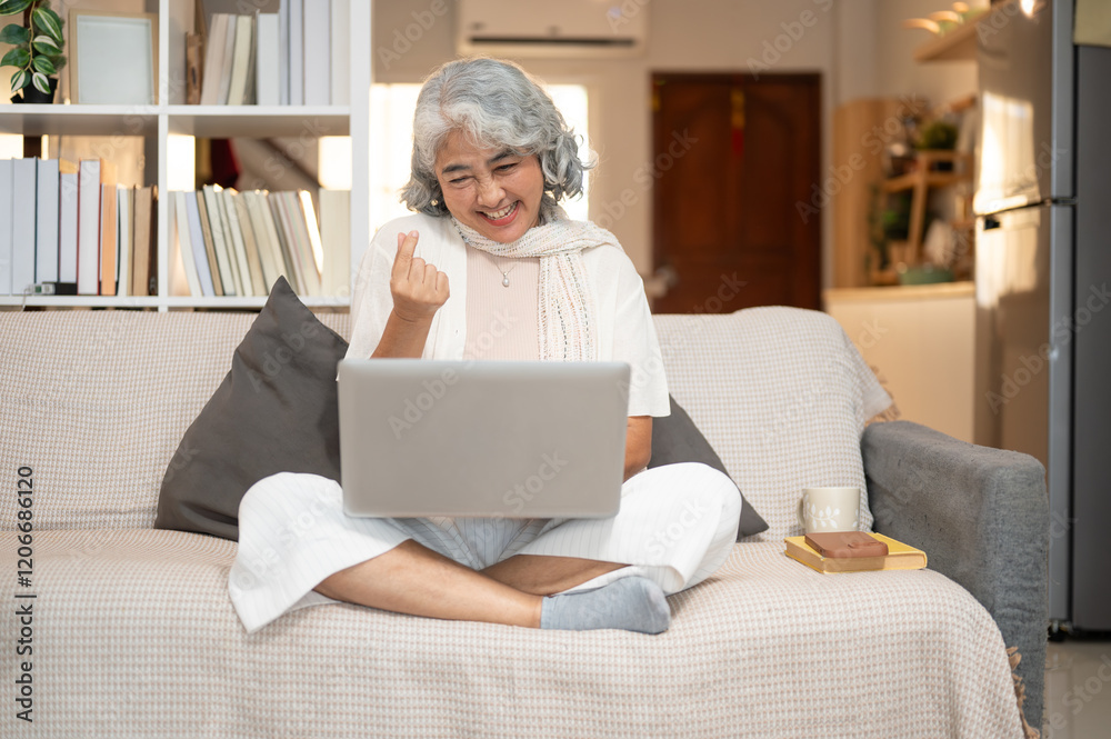 A happy Asian senior woman enjoys talking on a video call through her laptop while resting on a sofa A happy Asian senior woman enjoys talking on a video call through her laptop while resting on a sofa