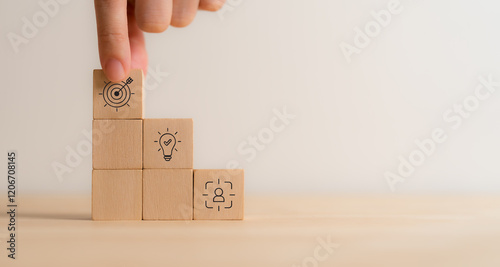 Strategic planning, business goals and achievement concept. Hand stacking wooden blocks with icons representing human resource development, innovation and target achievement. Business growth strategy.