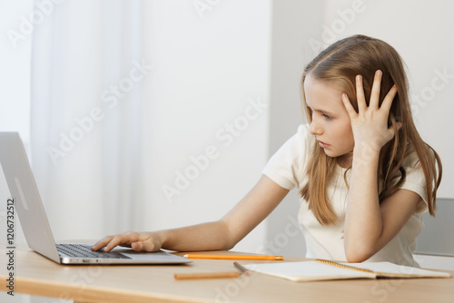 A young girl looking frustrated at her laptop, reflecting the challenges of online learning and concentration issues in a minimalistic, bright setting photo