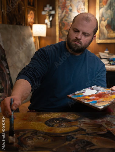  Religious icon painter man paints a new icon with brush at workshop photo