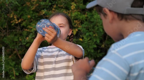 Girl, boy children kids drink water after active games in nature outside. Children replenish thirst, water balance in body, get rid of dehydration. Children kids greedily drink water from bottle. photo