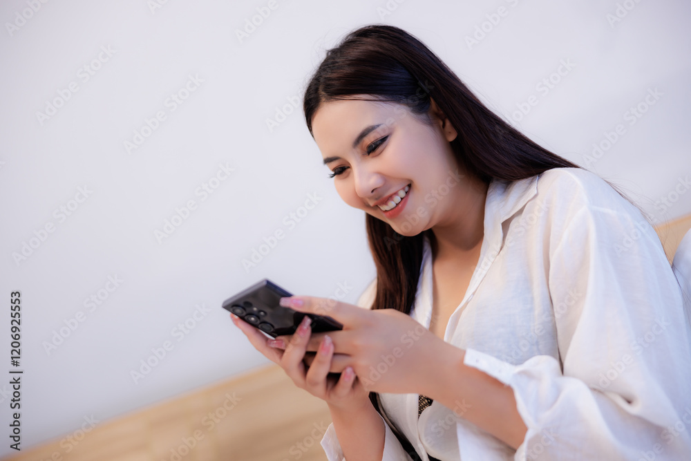 Naklejka premium asian woman sitting on bed using smartphone and happily