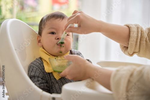 someone feeding a baby with a spoon in a high chair