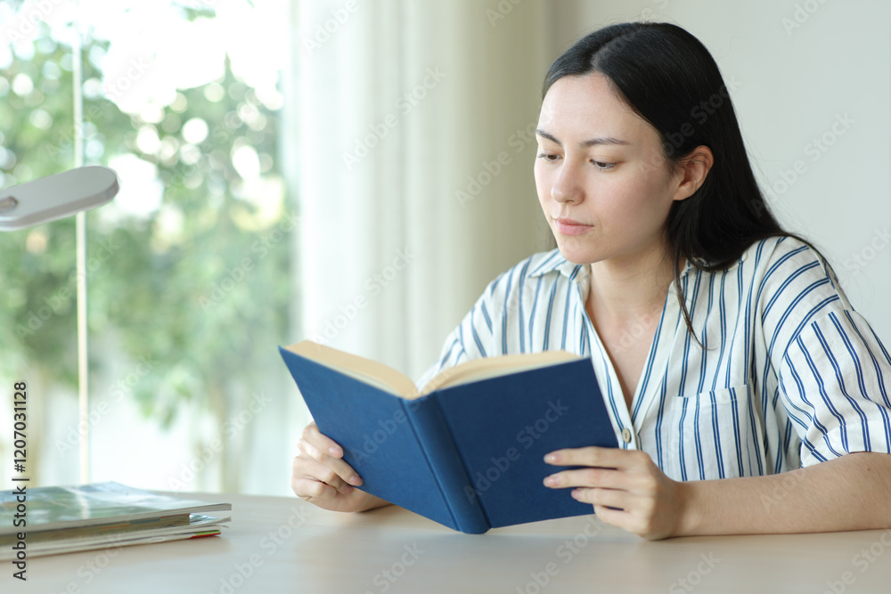 Serious asian woman reading a paper book on a desk Serious asian woman reading a paper book on a desk